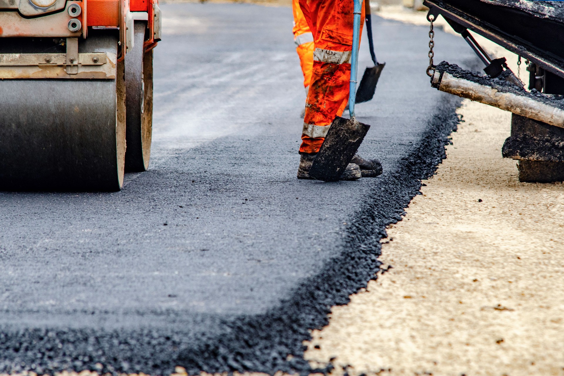 Construction workers in high-visibility gear are applyin gfresh hot asphalt to roadway surface